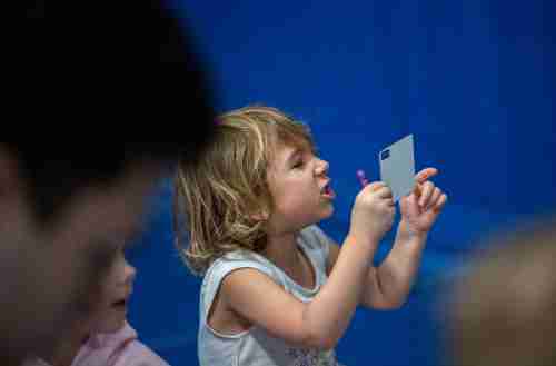 A small child makes a face at a card while holding a purple crayon.